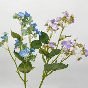 Op de afbeelding: Twee kunstmatige bloemstelen met blauwe en paarse hortensia bloemen. De stelen zijn groen en hebben kleine bladeren.