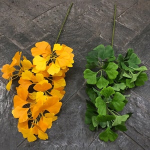 以下が含まれることがあります： 黄色の葉と緑色の葉の2本の銀杏の葉の茎。茎は灰色のタイル張りの表面にあります。