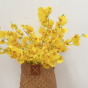 Könnte beinhalten: Ein Strauß gelber Orchideenblüten in einem geflochtenen Korb mit einem braunen Ledergriff.