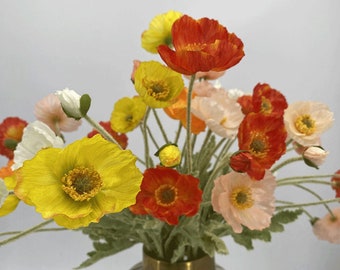 May include: A bouquet of artificial poppies in a variety of colours, including red, orange, yellow, pink, and white. The flowers are arranged in a vase with green foliage.