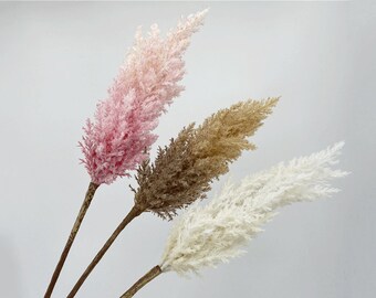 May include: Four decorative faux pampas grass stems in shades of pink, brown, and white. The stems have a feathery texture and are arranged against a white background. The stems are approximately 30 inches long.
