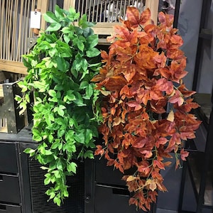 May include: Two artificial hanging plants, one with green leaves and one with orange leaves. The plants are hanging from a black metal shelf.
