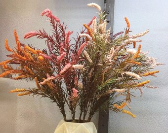 May include: A bouquet of artificial flowers in a vase. The flowers are in shades of pink, orange, and white. The flowers are arranged in a vase with a textured surface.