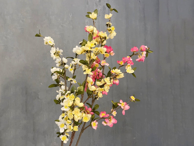 May include: A bouquet of artificial flowers with pink, yellow, and white blossoms. The flowers are arranged on a branch-like stem.