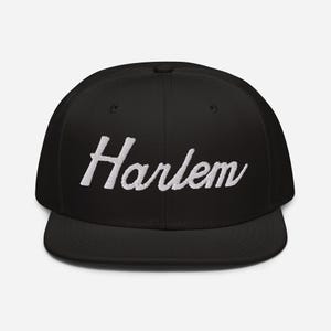 May include: A black and white baseball cap with the word "Harlem" embroidered in white on the front.