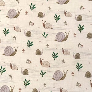 May include: A light beige fabric featuring a repeating pattern of small snails with lavender shells and brown bodies, interspersed with tiny green leafy sprigs and small brown clover-like plants scattered across the surface.