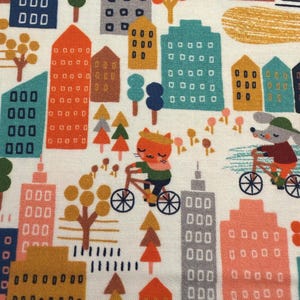 May include: Fabric with a repeating pattern of colorful buildings, trees, and cyclists. The buildings are various colors, including orange, teal, and gray. A cat and a mouse are riding bicycles. The background is white.