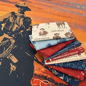 May include: A stack of fabric squares featuring John Wayne imagery and quotes, in shades of blue, red, and cream. The background shows a large poster with a cowboy illustration and the word "Starring". The fabrics have cowboy-themed patterns.