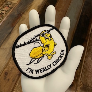 May include: White embroidered patch with a yellow cartoon chicken wearing sunglasses and riding a snowmobile. The text "I'm Weally Chicken" is embroidered in black around the edge of the patch.