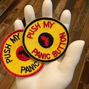 May include: Two yellow embroidered patches with red and black stitching. The patches are round and have the text "Push My Panic Button" on them.