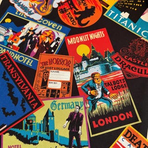 May include: A black fabric featuring a repeating pattern of colorful vintage-style travel stickers. Designs include labels for Hotel Von Frankenstein, Transylvania, Moonlit Nights at Talbots Lodge, The Horror of Lost Luggage, and Tokyo.