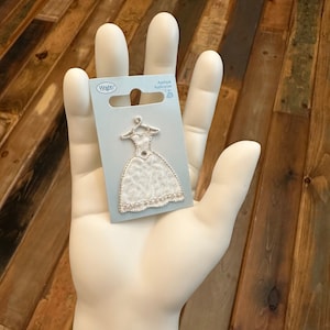 May include: White iron-on applique of a wedding dress with a single rhinestone embellishment. The applique is on a blue card with the text "Applique Applicacion 1 pc" and the Wright's brand logo.