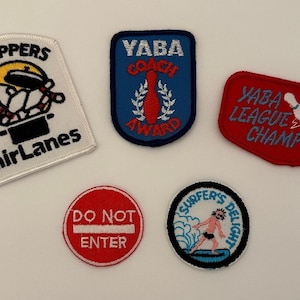 May include: Five embroidered patches with various designs. A white patch with a bowling pin design and the text "Pin Poppers Fair Lanes". A blue patch with a bowling pin design and the text "Yaba Coach Award". A red patch with a bowling ball design and the text "Yaba League Champion". A red circle with the text "Do Not Enter". A blue and white patch with a surfer design and the text "Surfers Delight".