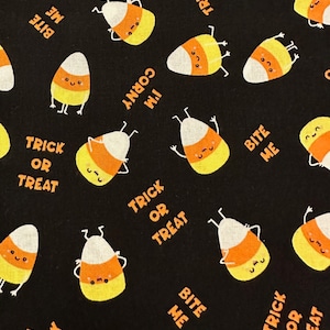 May include: Black fabric with a repeating pattern of orange and yellow candy corn with smiling faces. The candy corn has the text "Trick or Treat" and "Bite Me" on it.