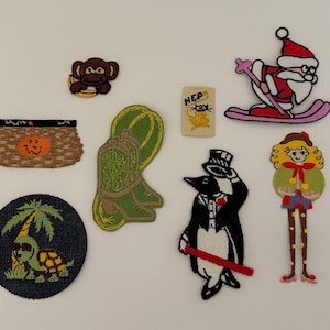 May include: A collection of ten embroidered iron-on patches featuring various designs, including a cowboy boot, a penguin, a turtle, a pumpkin, a monkey, a Santa Claus, a girl with pigtails, and a frog.