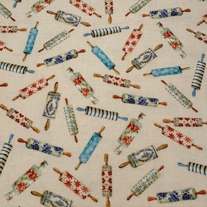 May include: A beige fabric with a repeating pattern of colorful rolling pins. The rolling pins have various designs, including blue and white floral patterns, red and white floral patterns, and blue and white stripes. The text "Jacobs & Bros. Home Bakery" is visible on some of the rolling pins.