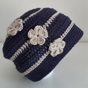 May include: A navy blue crocheted hat with white stripes and beige crocheted flower embellishments.