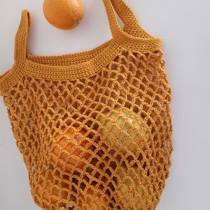 May include: A mustard yellow crocheted mesh bag filled with oranges and lemons. The bag has two handles and is made of a thick, durable yarn.