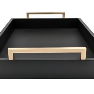 May include: A black rectangular serving tray with two gold metal handles. The tray is made of wood and has a smooth finish.