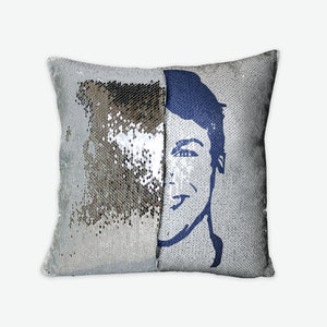 May include: A silver sequin pillow with a blue silhouette of a person's face on one side.