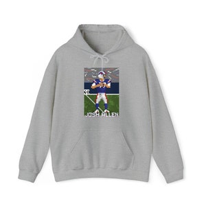 K&ouml;nnte beinhalten: Ein grauer Hoodie mit einem Pixelbild eines Footballspielers in einem blau-roten Trikot. Der Text "JOSH ALLEN" ist unter dem Bild gedruckt.