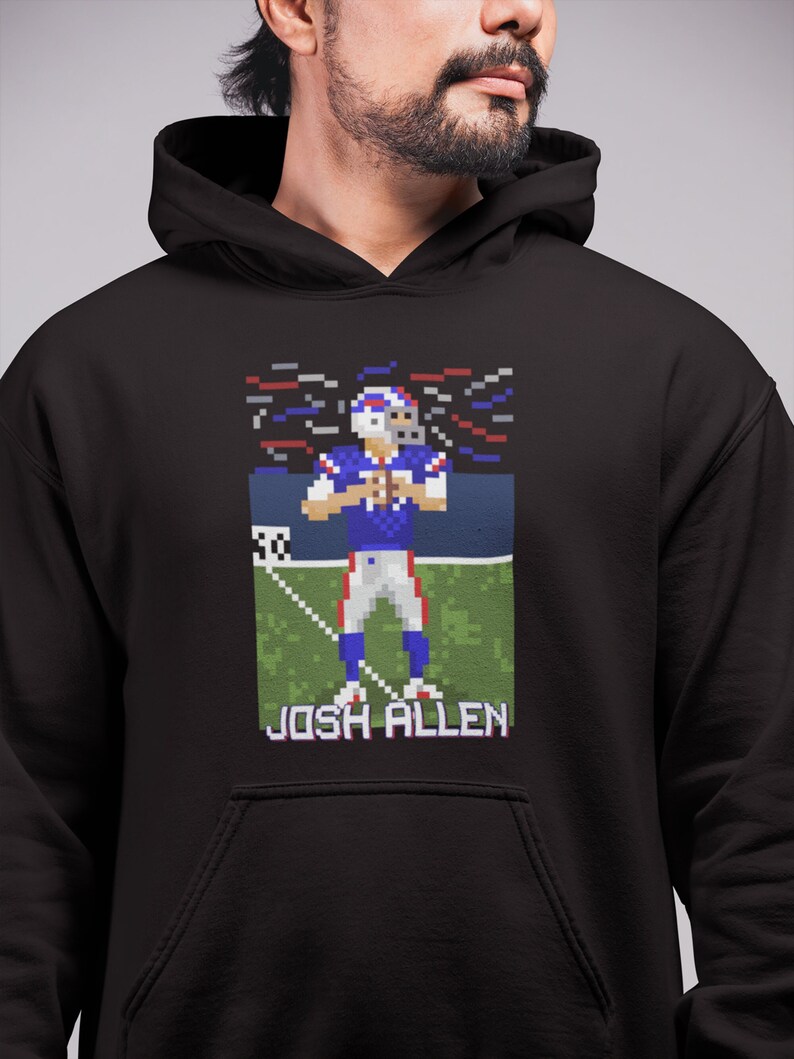 K&ouml;nnte beinhalten: Schwarzer Hoodie mit einem Pixelbild eines Footballspielers in einem blau-roten Trikot. Der Spieler h&auml;lt einen Football und der Text "JOSH ALLEN" befindet sich unter dem Bild.