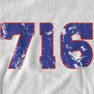 May include: A white t-shirt with a blue and red distressed number "716" printed on the front.