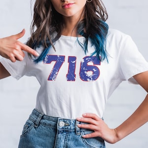 May include: A white t-shirt with the number "716" printed in blue with a red outline. The numbers have a distressed, vintage look.