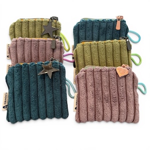 May include: A collection of small, corduroy-textured coin purses in various colors, including teal, olive green, and mauve. Each purse has a zipper closure, a small charm, and a wrist loop. The purses are arranged on a white background.