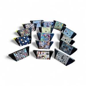 May include: A collection of cosmetic bags with various cartoon character designs. The bags have a black base with colorful patterned tops and gold or yellow zippers. The designs include characters from popular animated shows and movies.