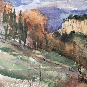 K&ouml;nnte beinhalten: Aquarellmalerei einer Landschaft mit einem Gebirge im Hintergrund, einer Felswand im Mittelgrund und einem Feld mit gr&uuml;nem Gras im Vordergrund. Das Gem&auml;lde ist in Blaut&ouml;nen, Gr&uuml;n, Braun und Wei&szlig; gehalten.