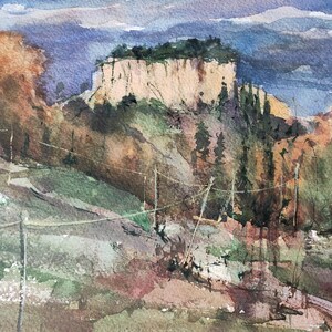 K&ouml;nnte beinhalten: Ein Aquarellbild einer Landschaft mit einer Klippe im Vordergrund und einem Gebirge im Hintergrund. Die Klippe ist hellbraun und hat ein paar B&auml;ume, die darauf wachsen. Das Gebirge ist hellblau und von einem leichten Nebel bedeckt. Das Bild ist in einem realistischen Stil gemalt.
