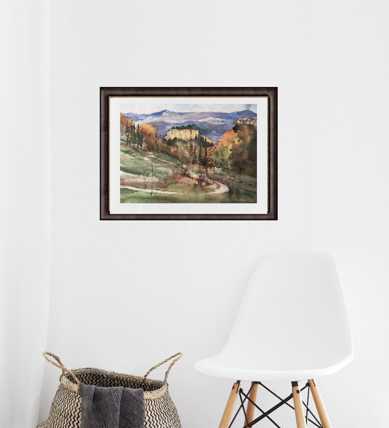 K&ouml;nnte beinhalten: Ein Aquarellbild einer Landschaft mit einer kurvigen Stra&szlig;e, die zu einem Bergdorf f&uuml;hrt. Das Bild ist in einem dunkelbraunen Rahmen gerahmt.