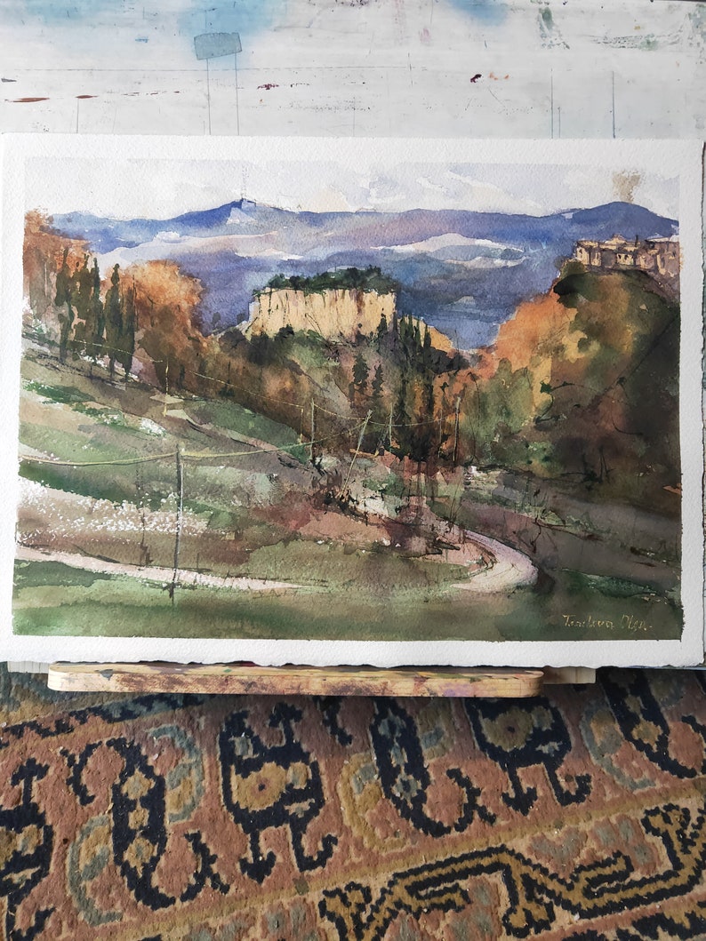 K&ouml;nnte beinhalten: Aquarellmalerei einer Landschaft mit einer Felswand, B&auml;umen und einer kurvigen Stra&szlig;e. Das Gem&auml;lde ist in Gr&uuml;nt&ouml;nen, Braun- und Blaut&ouml;nen gehalten. Die Unterschrift des K&uuml;nstlers ist unten rechts sichtbar.