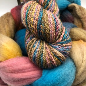 May include: A close-up of a variety of yarn in different colors, including blue, pink, yellow, and brown. The yarn is arranged in a circular pattern, with the ends of the yarn overlapping.