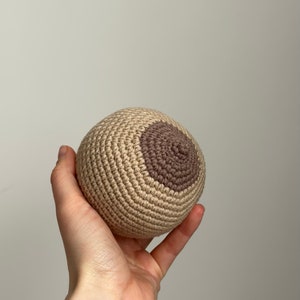 以下が含まれることがあります： 中央に茶色の円がある、かぎ針編みで作ったボール。ボールはベージュで、表面がざらざらしている。