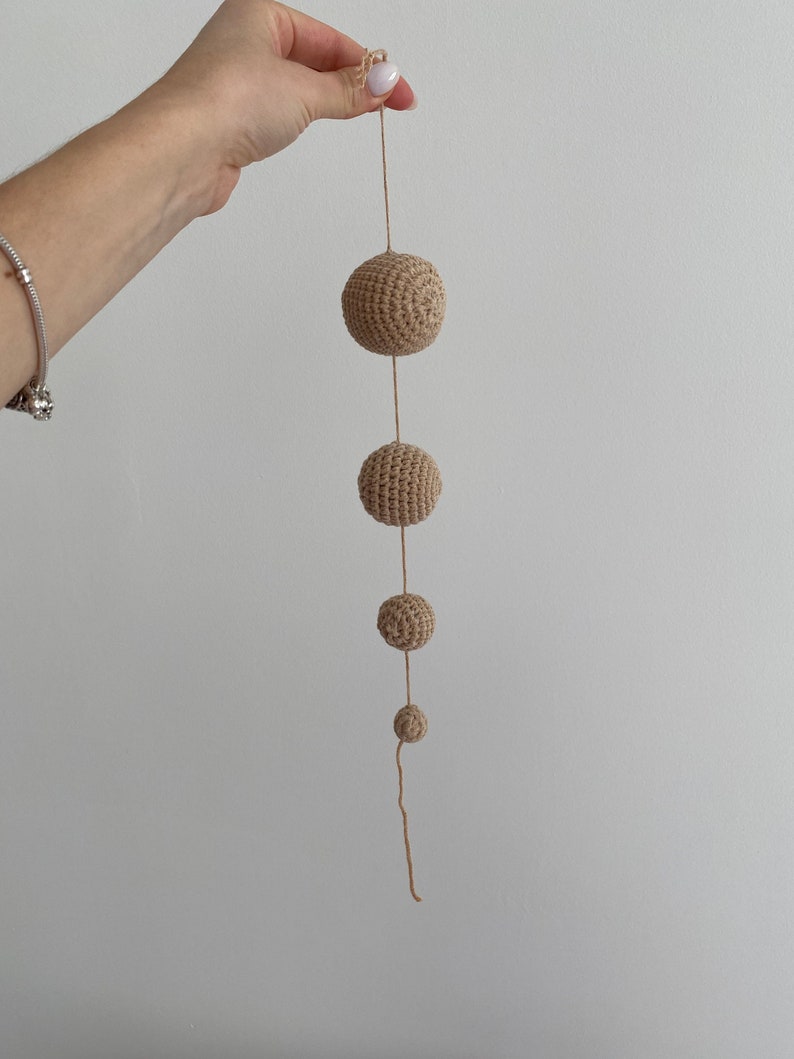 May include: A string of five beige crocheted balls of varying sizes hanging from a beige string.
