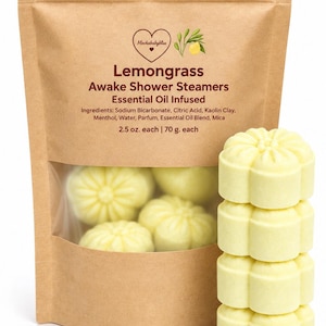 May include: A brown paper pouch labeled Lemongrass Awake Shower Steamers Essential Oil Infused with a clear window showing pale yellow flower-shaped tablets. A stack of four identical yellow flower-shaped shower steamers sits beside the pouch.