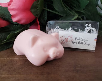 May include: Pink pig-shaped goat milk soap in a clear plastic box with a white paper label that reads "Pink Sugar Goat Milk Soap".