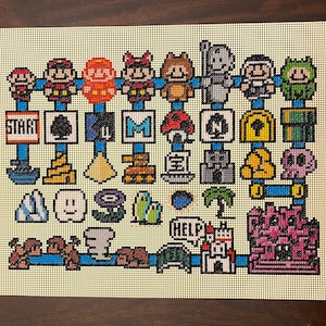 Op de afbeelding: Een kleurrijk kruissteekpatroon met personages en objecten uit de Super Mario Bros. videogame-serie. Het patroon bevat Mario, Luigi, Toad, Goomba's, een paddenstoel, een ster, een vraagtekenblok, een pijp en een kasteel.