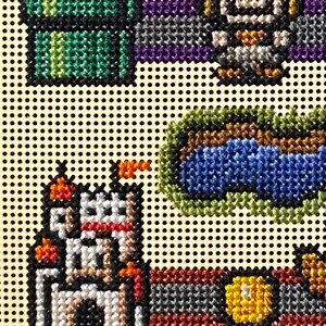 May include: Needlepoint design featuring pixelated images of a green pipe, a character, a castle, and a coin. The design uses various colours including green, blue, white, orange, and yellow. The background is a light tan colour with black dots.