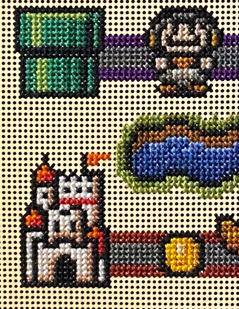 May include: Needlepoint design featuring pixelated images of a green pipe, a character, a castle, and a coin. The design uses various colours including green, blue, white, orange, and yellow. The background is a light tan colour with black dots.