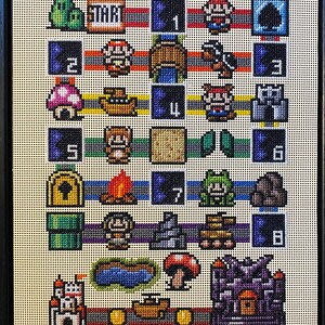 May include: A framed needlepoint depicting a pixelated video game board with various characters and elements. The board includes numbers, a start marker, and iconic game imagery in a grid-like pattern. The colour palette includes red, blue, green, and yellow.