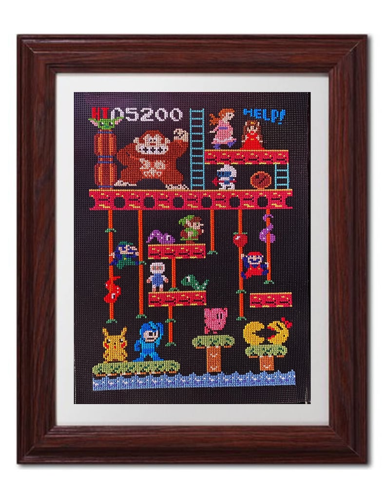 Puede incluir: Una obra de punto de cruz enmarcada que representa una escena de videojuego retro. La escena presenta un gorila grande, una escalera y varios personajes de videojuegos cl&aacute;sicos, incluidos Mario, Pac-Man y Pikachu. El texto "HELP!" y "05200" son visibles en la obra.