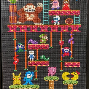 Puede incluir: Un dise&ntilde;o de punto de cruz pixelado con personajes de videojuegos populares. El dise&ntilde;o incluye un gorila marr&oacute;n grande, un robot azul, un Pikachu amarillo, un Kirby rosa y un personaje verde de Mario. El texto "HI 05200 HELP?" se muestra en la parte superior del dise&ntilde;o.