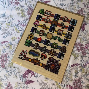May include: A framed cross-stitch depicting a pixelated design inspired by a classic video game. The artwork includes iconic characters, level elements, and the word "START". The colour palette includes red, green, blue, brown, and yellow.