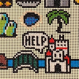 Op de afbeelding: Een kruissteekpatroon met een wit kasteel, een groene brug, een blauw meer, een palmboom en een spreekballon met de tekst "HELP".