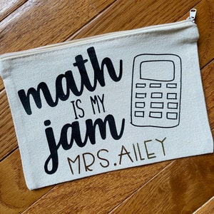 May include: A white canvas zippered pouch with the text "math is my jam" and a black and white illustration of a calculator. The text "MRS. AILEY" is written below the calculator.