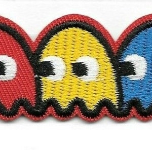 May include: A set of embroidered iron-on patches featuring the classic Pac-Man characters. The set includes one yellow Pac-Man and four ghosts: red, yellow, blue, and pink.