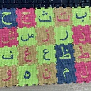 May include: A set of colorful foam puzzle pieces featuring the Arabic alphabet. Each piece has a different letter in a bold, white font. The letters are arranged in rows, with each row having a different color scheme.